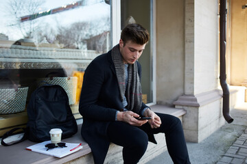 Man using smartphone on stone parapet in street