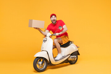 Delivery man in red cap tshirt uniform driving moped motorbike scooter hold cardboard box isolated on yellow background studio Guy employee working courier Service quarantine pandemic covid-19 concept © ViDi Studio