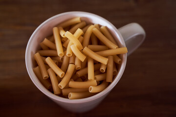 Yellow pasta lie in a white plate with a handle brown table. Close-up. Top view.