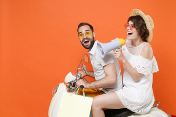 Side view of funny young couple friends guy girl in hat glasses driving moped isolated on orange...