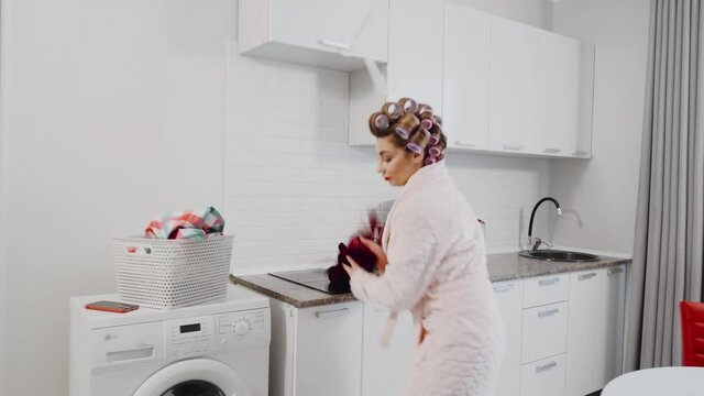 An agitated woman in a panic grabs the dress and wipes the water while the water flows from under the washing machine in the kitchen. A housewife who has a leak in the kitchen. Woman having washer