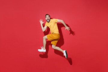 Fototapeta na wymiar Side view of excited young bearded man guy in casual yellow t-shirt posing isolated on red background studio portrait. People lifestyle concept. Mock up copy space. Jump like running, spreading hands.