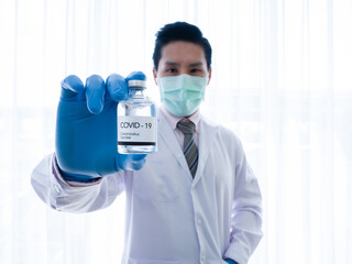 Asian man doctor wear face mask, white gown and holding covid-19 or corona virus vaccine in glass bottle for protect patient from flu pandemic disease by injection in clean hospital or laboratory