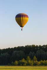 Obraz premium Kyiv, Ukraine - 06/26/2020: Hot air balloon in clear summer sky over trees. Yellow balloon on blue sky background. Bright geometric design. Summer leisure. Hot air balloon in flight in the morning.