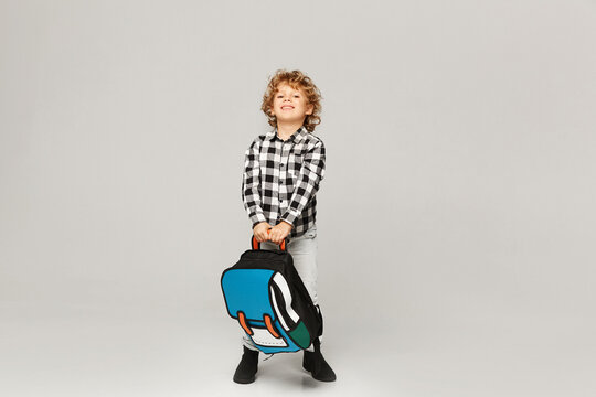 Back to school. A funny little boy from elementary school posing with a backpack over white background, isolated