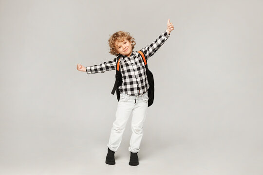 A little schoolboy is happy to start the school year. Happy kid with a backpack posing at the white background, isolated.