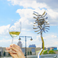 Glass of white wine with reflection on the blurred cityscape and dramatic sky background. Space for text. Wine concept.