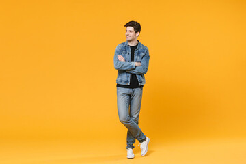 Fototapeta na wymiar Smiling young man guy 20s wearing casual denim clothes posing isolated on yellow background studio portrait. People emotions lifestyle concept. Mock up copy space. Holding hands crossed looking aside.