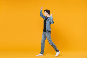 Fototapeta na wymiar Side view of excited young man guy wearing casual denim clothes posing isolated on yellow background studio portrait. People lifestyle concept. Mock up copy space. Expressive gesticulating with hands.