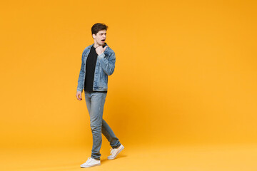 Fototapeta na wymiar Shocked young man guy 20s wearing casual denim clothes posing isolated on yellow wall background studio portrait. People sincere emotions lifestyle concept. Mock up copy space. Pointing thumb aside.