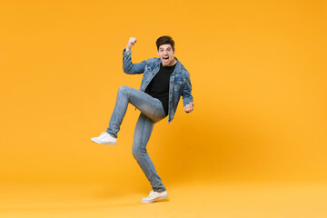 Fototapeta na wymiar Screaming young man guy wearing casual denim clothes posing isolated on yellow wall background studio portrait. People emotions lifestyle concept. Mock up copy space. Rising leg, doing winner gesture.