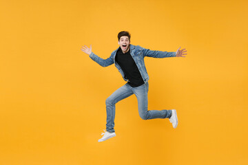 Surprised young man guy wearing casual denim clothes posing isolated on yellow background studio portrait. People sincere emotions lifestyle concept. Mock up copy space. Jumping, spreading hands legs.