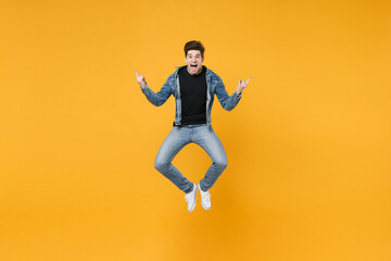 Obraz premium Screaming young man guy wearing casual denim clothes posing isolated on yellow wall background studio portrait. People lifestyle concept. Mock up copy space. Jumping, depicting heavy metal rock sign.