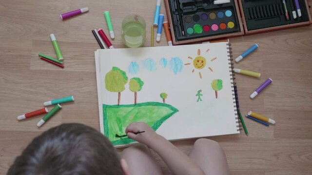 Child coloring a drawing of a field with a green watercolor