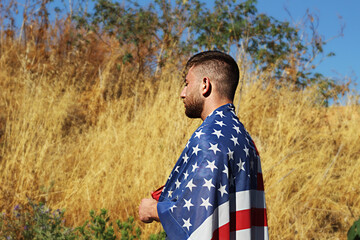 American teenager is stands on an American field with his eyes closed and flag USA on the back. Concepts: Independence Day United States, Veterans Day or  Memorial Day in USA