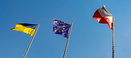 Flags of Ukraine of the European Union and Poland. Three flags on the background of a beautiful blue sky