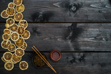 Round bowl of tea and tongs with dry bergamot frame on black wooden table. View from above