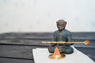 Fgurine King of monkey sitting with spoon on light fabric and dark wooden table and meditete with chinese incense 