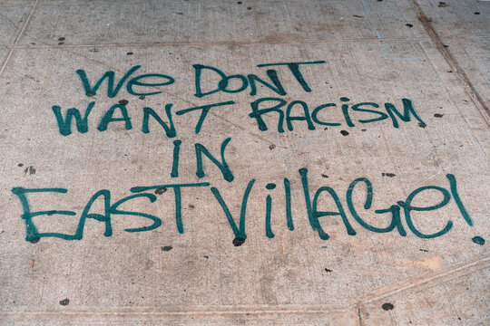 We Don't Want Racism in East Village, NYC  graffiti sprayed over the sidewalk street.