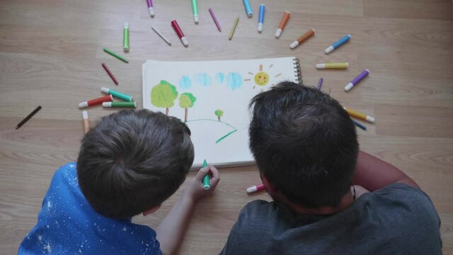 Child drawing with his father with colored markers on a pad on the floor