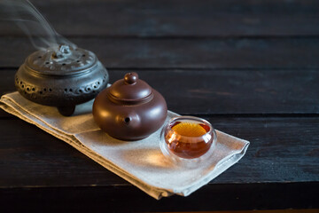 Teapot, incense and bowl with tea on light fabric and black wooden table