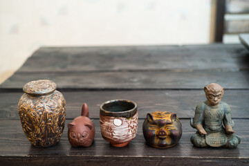 Different tea decorative chinese figurines: king of monkey, cat, pig and tea bowls on dark wooden table