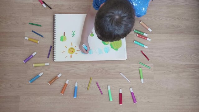 Child drawing with colored markers on a pad on the floor