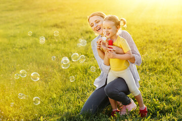 Mother and daughter spend family time blowing bubbles in the evening sunset rays