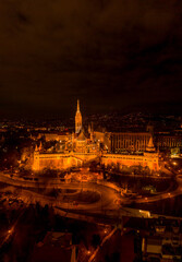 Fototapeta premium Aerial drone shot of Matthias Church with lights on Buda Hill in Budapest evening