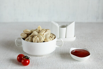 Composition on a light background, a Cup with ravioli dumplings with meat filling and cherry tomatoes. The concept of cooking delicious food at home. Selective focus.
