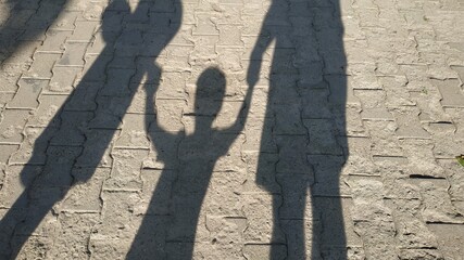Fototapeta na wymiar young family holding son's hands, shadows from the sun