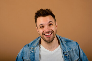 Handsome man standing and smiling isolated on light brown studio background. Male half-length portrait. The human emotions, facial expression concept. Front view.