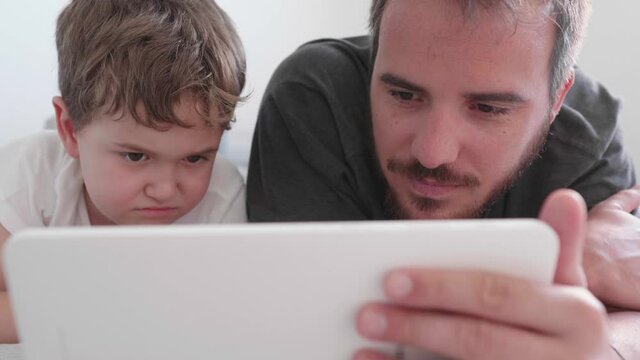 Child and parent lying there looking at the tablet and smiling