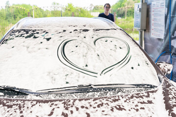 a heart is drawn on the car glass in foam at a car wash. the man in the background. symbol of respect for the car of the client