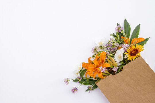 A bouquet of flowers in a craft bag on a white background. Flower delivery. Floral composition. Space for text. Spring background. Flat lay. Floristic. Postcard for the holiday.