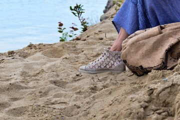 feet in shoes on the beach, woman sitting on the beach on a blurry background of sea