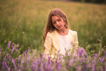 Fototapeta na wymiar Beautiful girl at sunset in a field with purple flowers. Lavender. The child walks and travels. Rest and games. Long haired girl