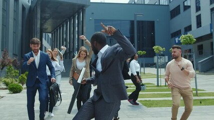 Happy motivated group of multi-ethnic young workers dancing with joy while walking on street celebrating day of employment. Success. Motivation. Victory. Business.