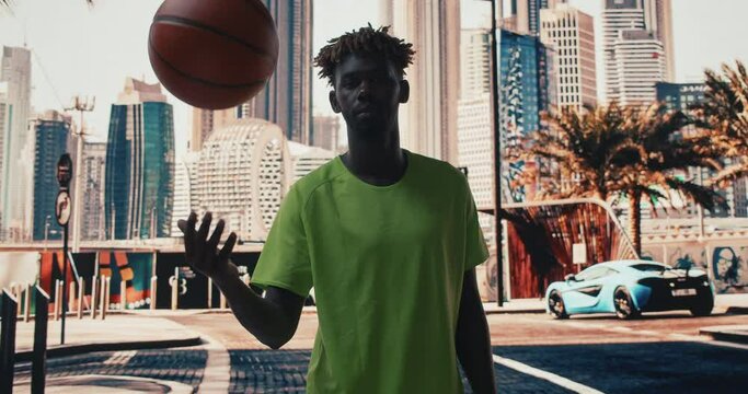 African american basketball player in rich Dubai street with skyscrapers. Young african ethnicity male doing some exercises with the ball. 