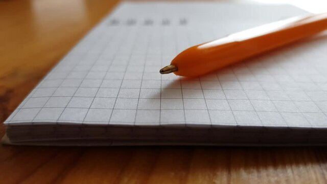 Orange ballpoint pen on a blank sheet of notepad, side view on a table