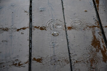 It is raining. Puddles on wooden flooring made of painted boards. Bouncing bizarre splashes. Circles diverge in water.