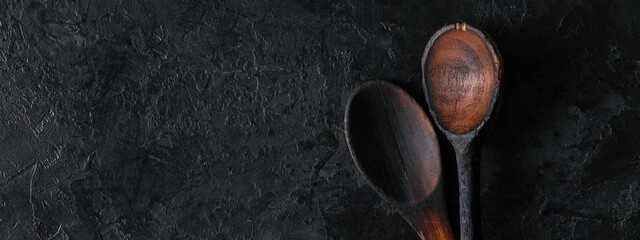 Two wooden spoons on a black concrete background with a copy of space. Old wooden spoons. Top view.