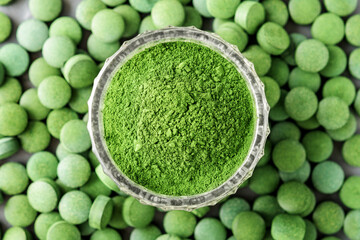Shredded chlorella or spirulina in a glass cup against a tablet background. Top view.