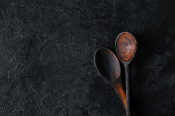 Two wooden spoons on a black concrete background with a copy of space. Old wooden spoons. Top view.
