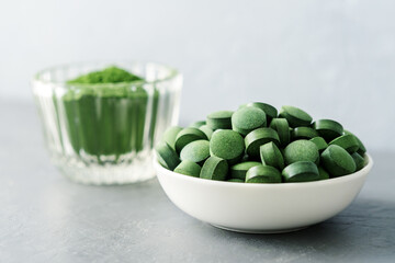 Chlorella or spirulina in the form of tablets and powder on a gray concrete background.