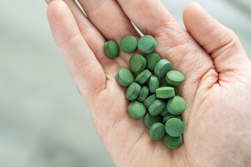 Hand with chlorella or spirulina tablets on grey background. Top view.