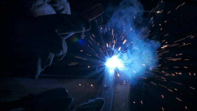 A welder lights up the room as he uses a welding torch for metal work.