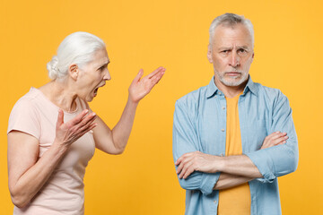 Angry irritated elderly gray-haired couple woman man in casual clothes posing isolated on yellow background studio. People lifestyle concept. Mock up copy space. Screaming swearing spreading hands.