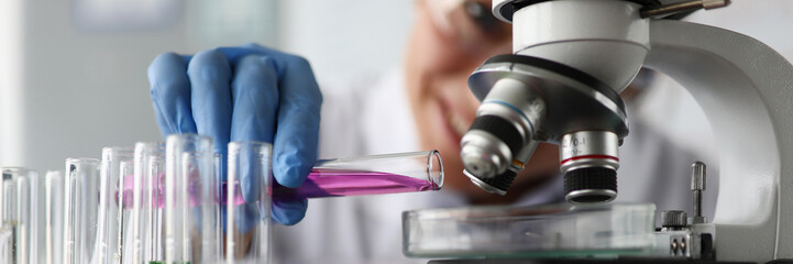 Close-up of professional chemist examining drug sample. Lab researcher investigating coloured liquid of chemical agent under microscope. Scientific research concept