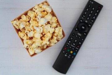 Top view of popcorn box and tv remote control on white wooden table